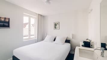Habitación de hotel con cama, mesita de noche con lámpara, ventana con cortinas y televisor montado en la pared.