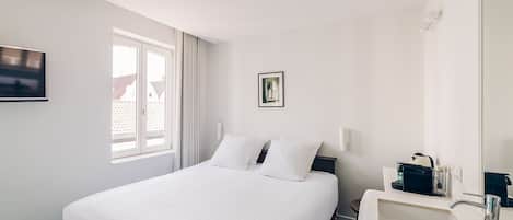 A hotel room with a bed, a bedside table with a lamp, a window with curtains, and a wall-mounted TV.