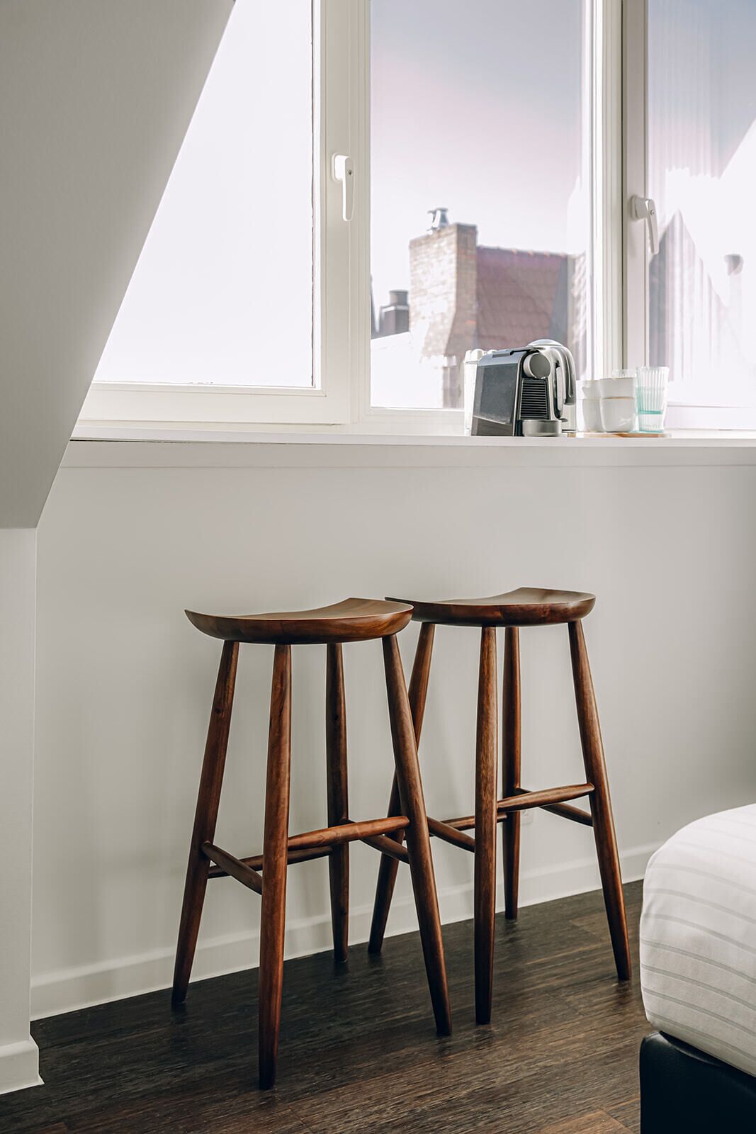 Una habitación con dos taburetes de madera, una ventana con vistas a edificios y un radiador en la pared.