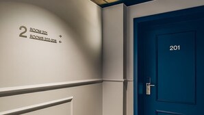 Un pasillo con un cartel en la pared que indica '2 ROOM 201' y 'ROOMS 202-208'.