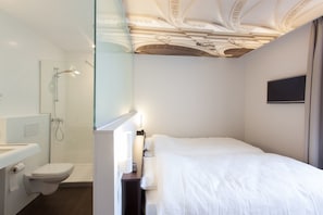 Un baño moderno con cabina de ducha de vidrio, un inodoro y una cama con ropa blanca.