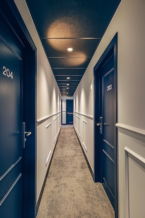 Corridoio di un hotel con porte numerate 204 e 203, pavimento rivestito di moquette e illuminazione a incasso.