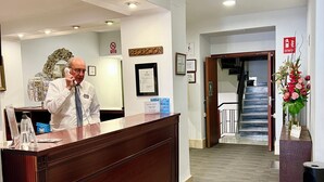 Una recepción con un hombre hablando por teléfono, un certificado en el marco en la pared y una escalera al fondo.