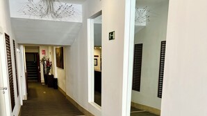 Un pasillo de hotel con piso alfombrado, paredes blancas y una lámpara en el techo.