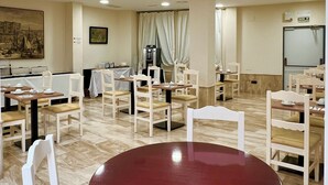 Un comedor con varias mesas y sillas, un cuadro grande en la pared, e iluminación empotrada en el techo.
