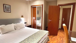 Una habitación de hotel con una cama grande, un escritorio con silla, un armario y un espejo.