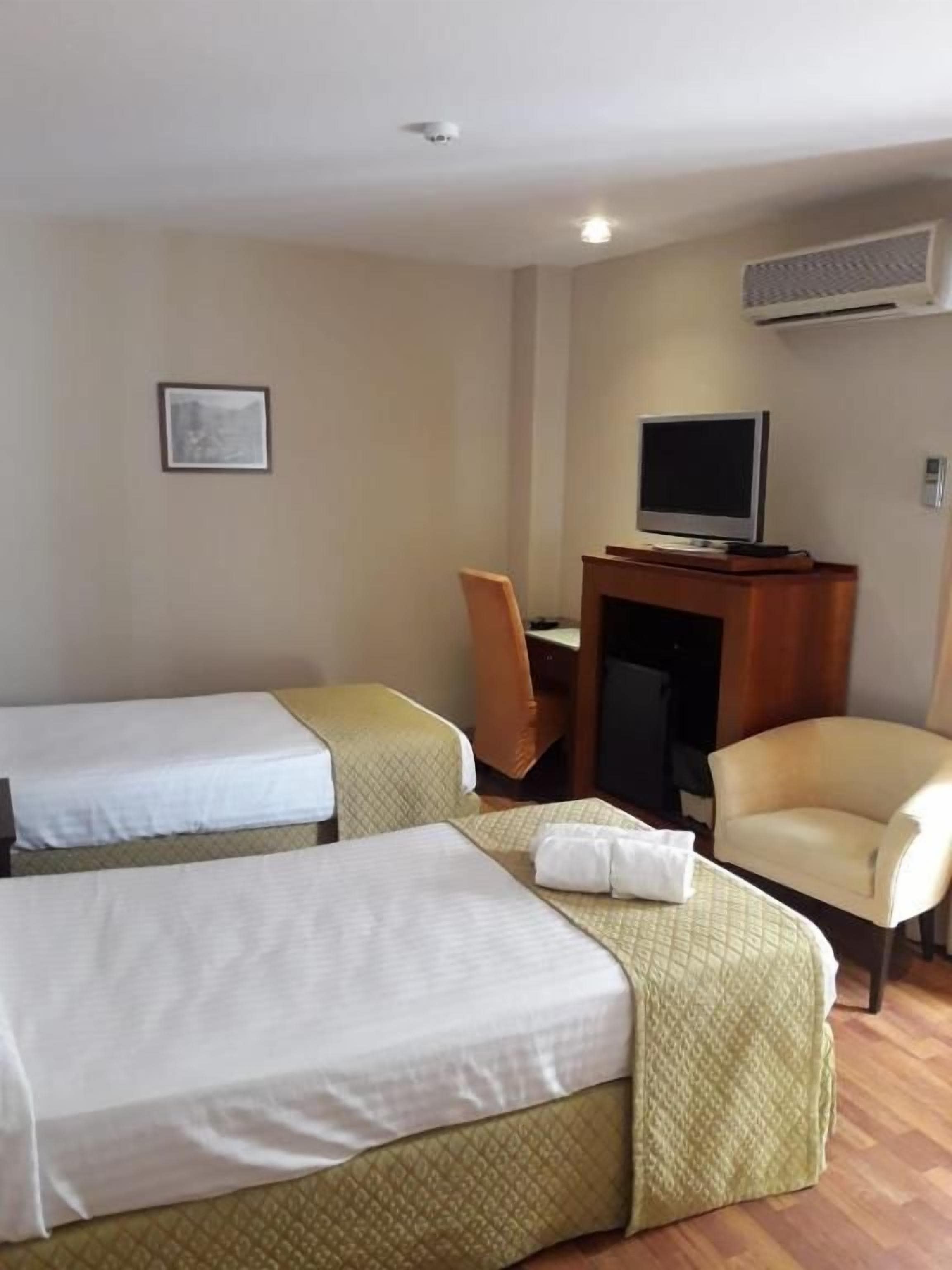 A hotel room with two beds, a television, a chair, and an air conditioning unit.