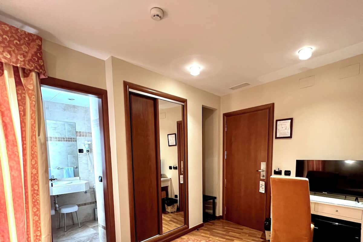 Une chambre d’hôtel avec un lit, un bureau, une chaise, une télévision et une salle de bain visible à travers une porte ouverte.