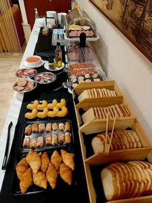 A buffet table with various food items including pastries, bread, and condiments.