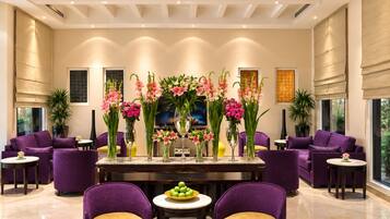 A modern lobby with a reception desk, purple seating, and floral arrangements.