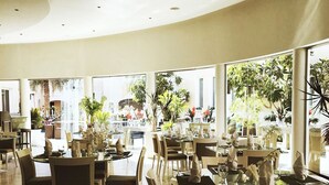 Een restaurant met ronde tafels en stoelen, grote ramen met uitzicht op de omgeving, en een gebogen plafond.