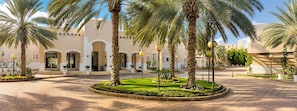 A courtyard with palm trees, a paved walkway, and a building with arched doorways. - Vivienda Hotel Villas, Turki Al Awwal (Riyadh)
