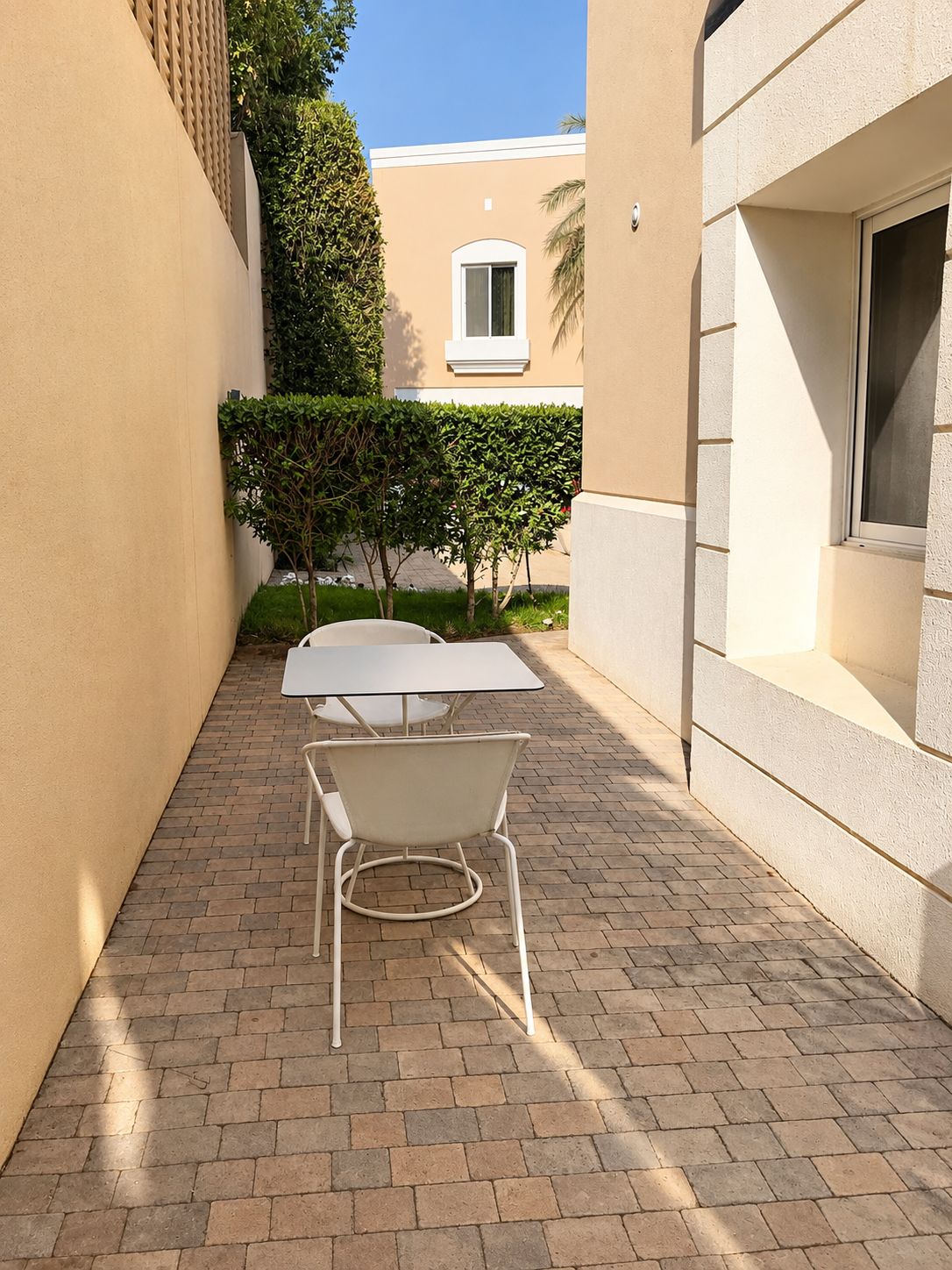 A patio with a white table and chairs, surrounded by a brick floor and beige walls.