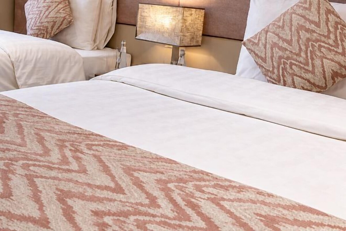 A hotel room with a bed, pillows, a nightstand, and a lamp.