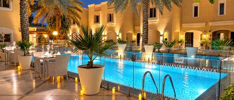 A swimming pool with a glass barrier, surrounded by palm trees and outdoor seating.