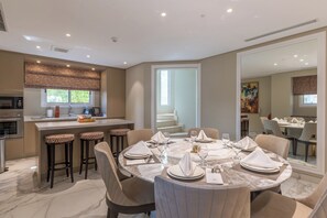A modern dining area with a marble table, bar stools, and a kitchen in the background.