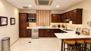 A modern kitchen with wooden cabinets, a stainless steel dishwasher, a microwave, and a sink. There is a bar area with stools and a small table with a coffee machine and cups.