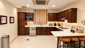 A modern kitchen with wooden cabinets, a stainless steel dishwasher, a microwave, and a sink. There is a bar area with stools and a small table with a coffee machine and cups. - Vivienda Hotel Villas, Turki Al Awwal (Riyadh)