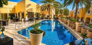 Un área de piscina con suelo de baldosas, rodeada de sillones de descanso y plantas en macetas.