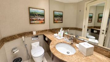 A modern bathroom with a marble sink, a toilet, a shower, and two framed landscape paintings on the wall.