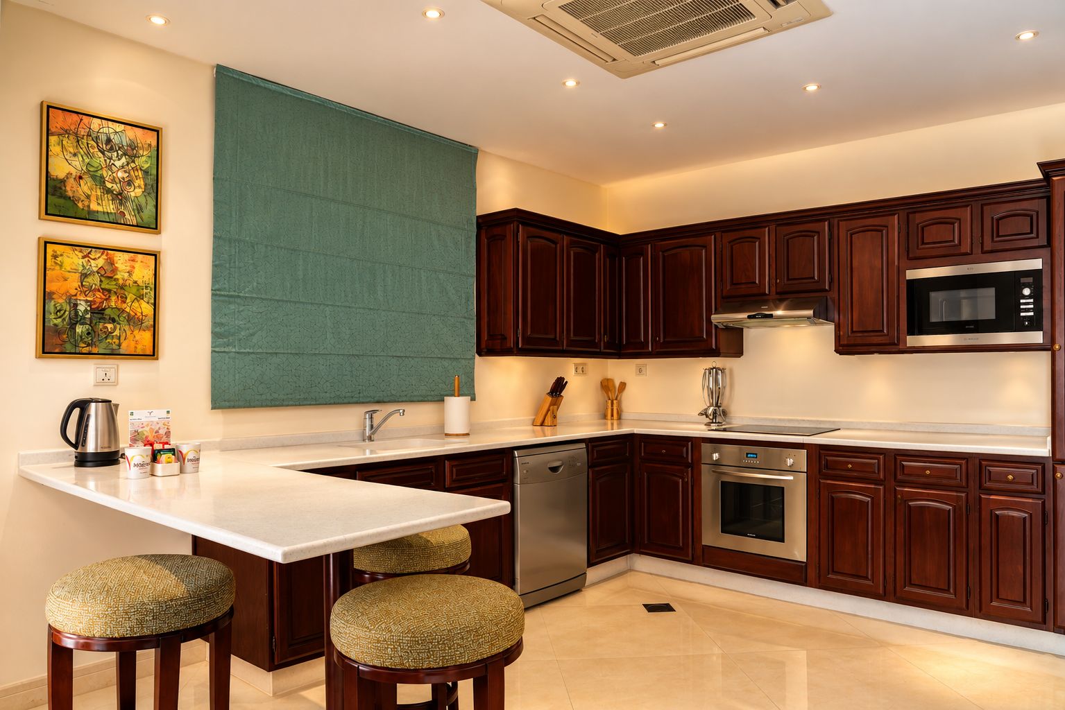 A modern kitchen with dark wooden cabinets, stainless steel appliances, and a white countertop. There are two stools with woven seats, a coffee maker, and a set of knives on the counter.
