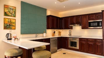 A modern kitchen with dark wooden cabinets, stainless steel appliances, and a white countertop. There are two stools with woven seats, a coffee maker, and a set of knives on the counter.