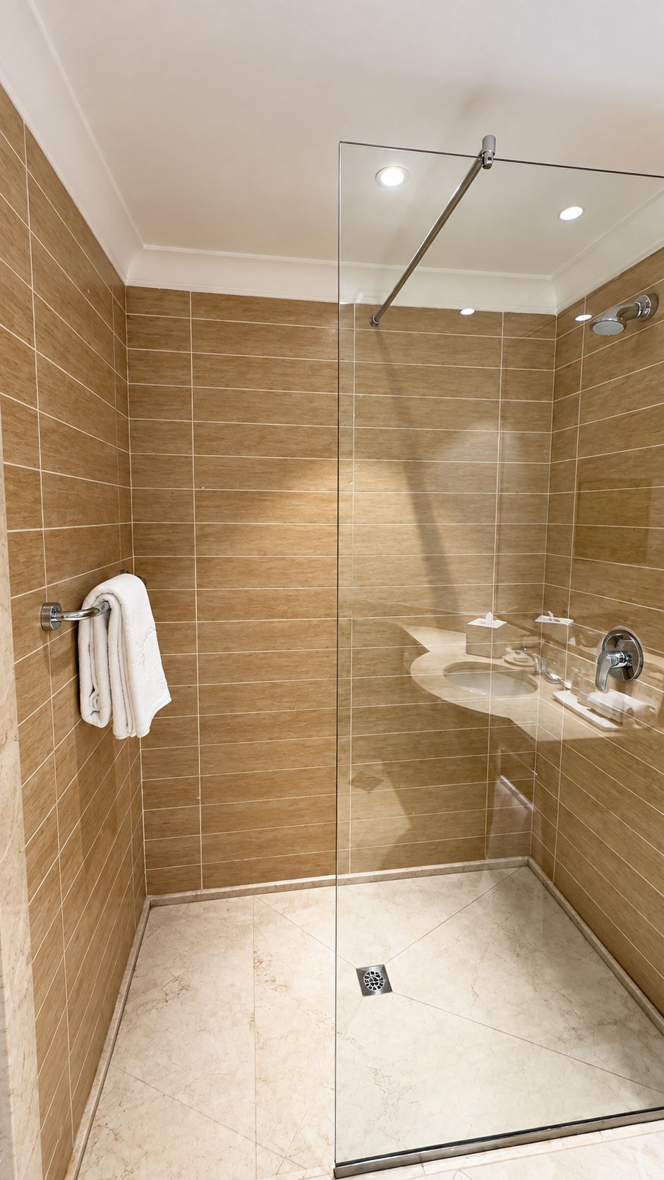 A modern shower with a glass door, a white towel hanging on a metal rack, and a sink with a mirror.