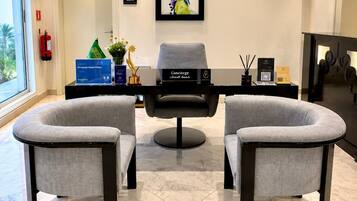 A modern reception area with two grey armchairs, a black sofa, a framed abstract painting, and a reception desk with a sign.