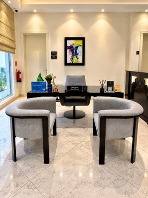A modern reception area with two grey armchairs, a black sofa, a framed abstract painting, and a reception desk with a sign. - Vivienda Hotel Villas, Turki Al Awwal (Riyadh)