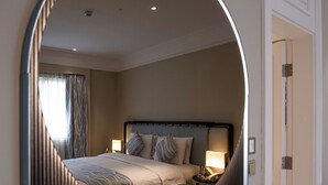 Een hotelkamer met een grote spiegel, een bed met kussens, een nachtkastje en een lamp.