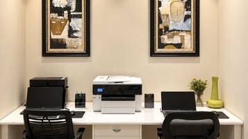 A modern office desk with two chairs, a printer, and two framed abstract paintings on the wall.