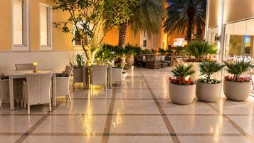 An indoor lobby with a checkered floor, wicker furniture, and potted plants.