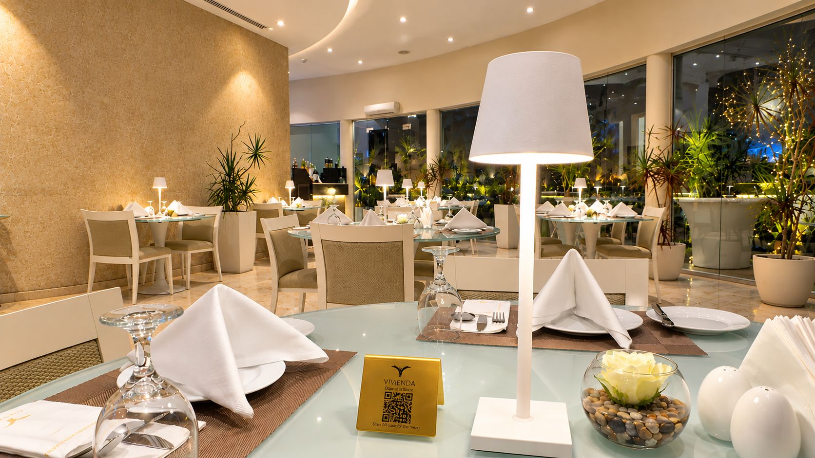 A well-lit dining area with tables set for service, a QR code for digital menu access, and a view of the outdoors through large windows.