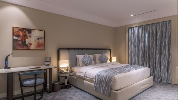 Ein Hotelzimmer mit Bett, Schreibtisch, Stuhl, Nachttischlampen und einem Bild an der Wand.
