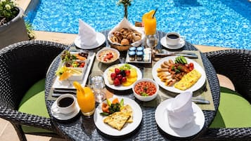Ein Esstisch mit Frühstücksangeboten, ein Pool im Hintergrund und Sitzgelegenheiten im Freien.