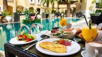 A dining table with breakfast items, a poolside setting, and a tropical garden view.