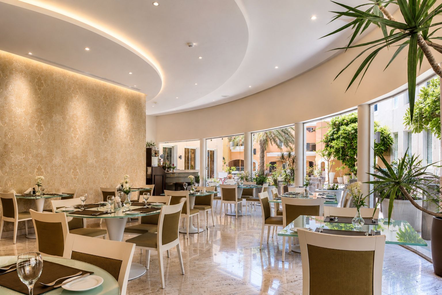 Un amplio comedor interior con varias mesas y sillas, ventanas grandes y plantas de interior.