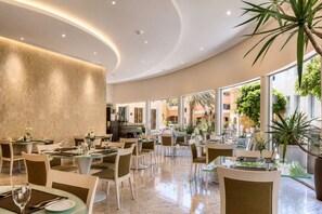 A spacious indoor dining area with multiple tables and chairs, large windows, and indoor plants. - Vivienda Hotel Villas, Turki Al Awwal (Riyadh)