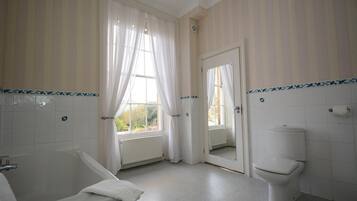 A bathroom with a bathtub, toilet, and a window with curtains.