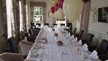 A long dining table set for a formal event, with chairs on both sides and balloons in the background.