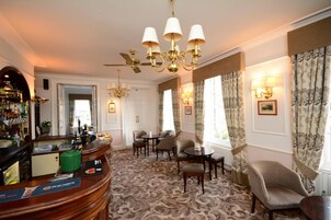 A hotel lobby with a bar area, seating, patterned carpet, and decorative lighting.