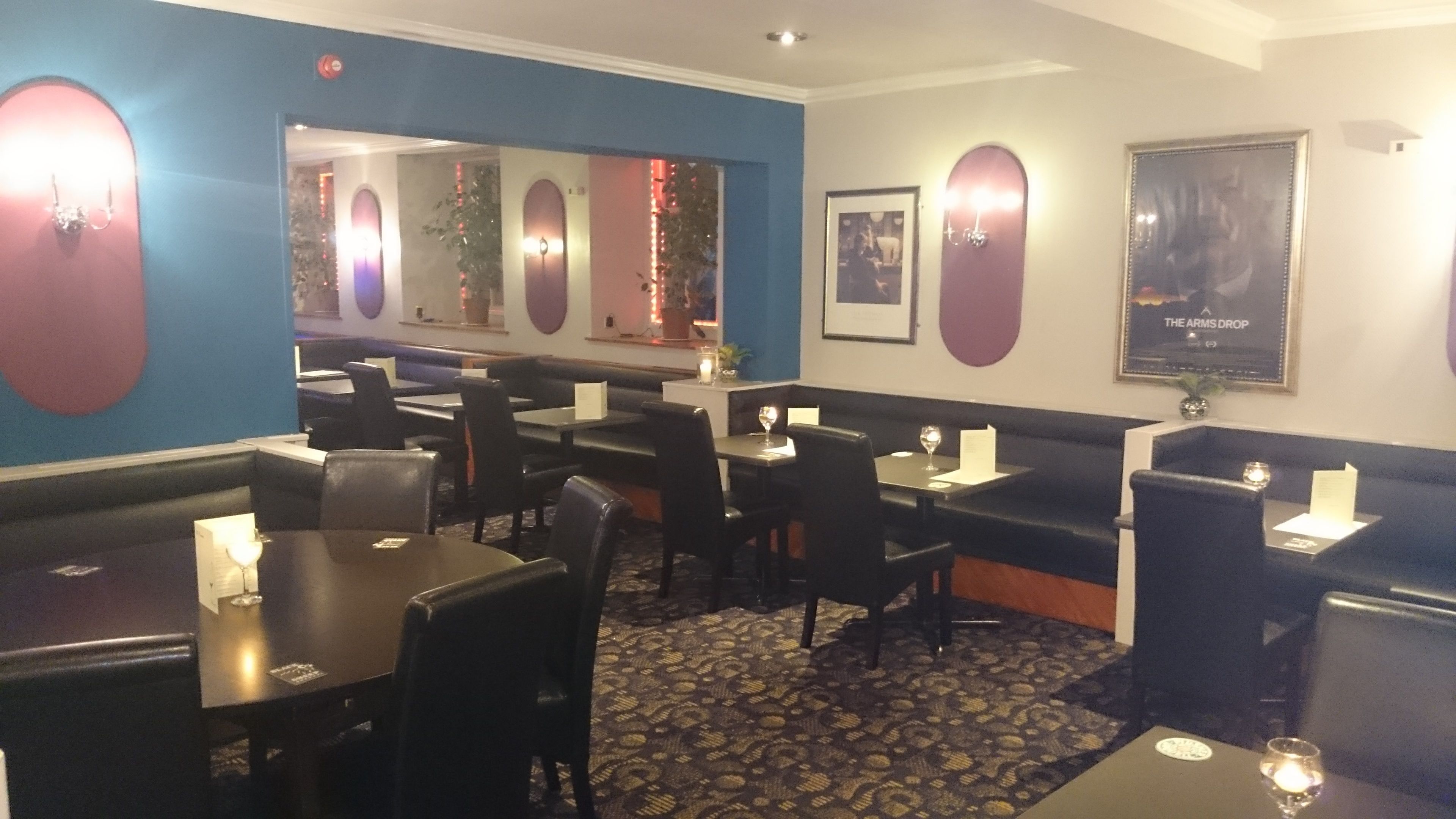 A restaurant interior with booths and tables, a patterned carpet, and wall-mounted lights.