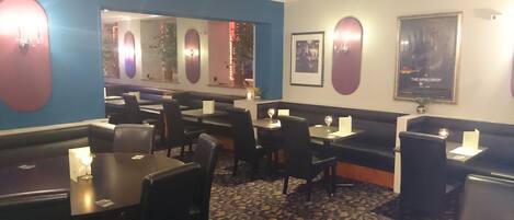 A restaurant interior with booths and tables, a patterned carpet, and wall-mounted lights.