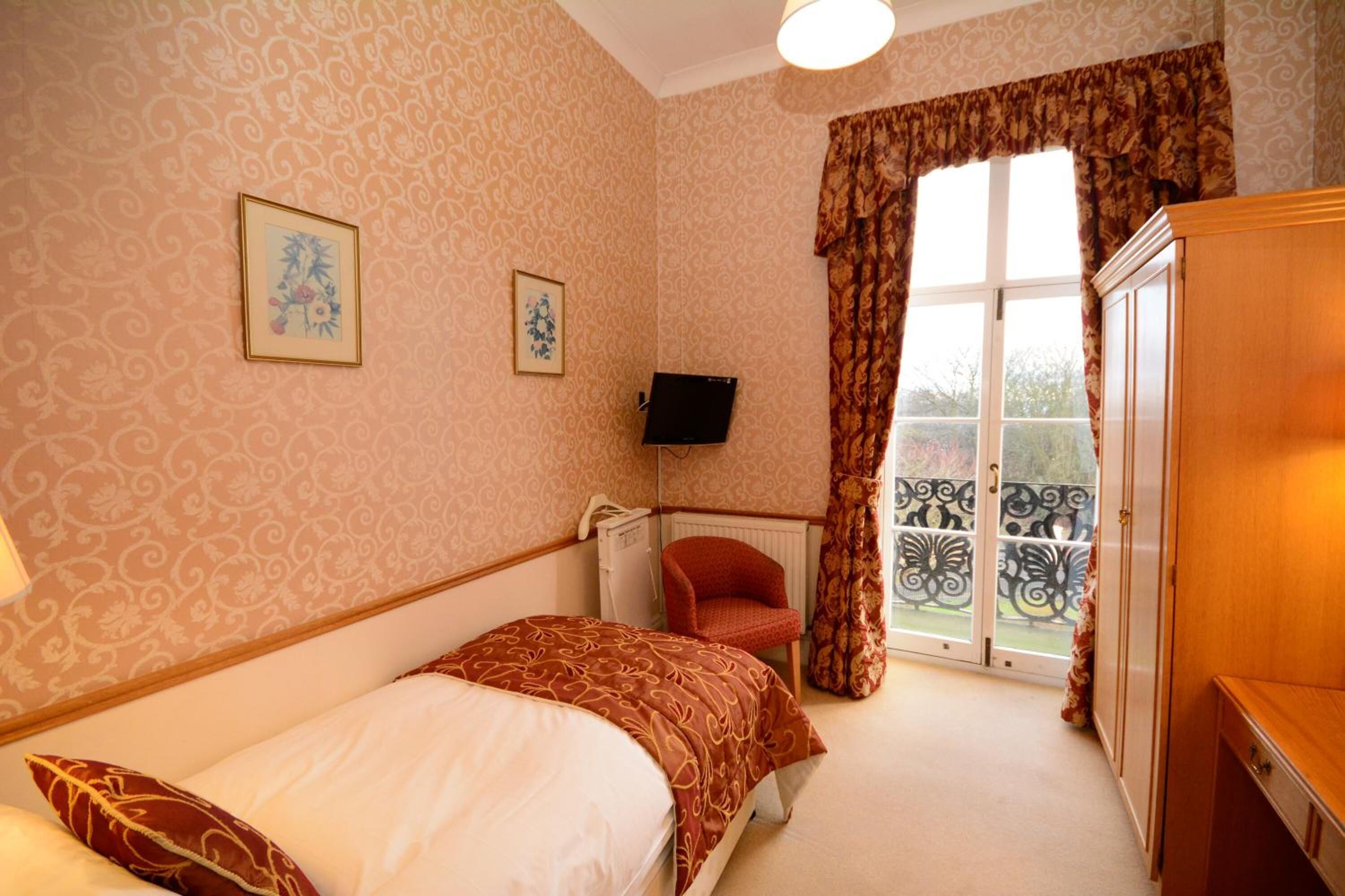 A bedroom with a bed, a chair, a TV, and a window with curtains.