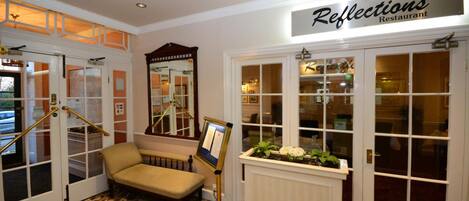 A reception area with a sign for 'Reflections Restaurant', a bench, a mirror, and a bulletin board.