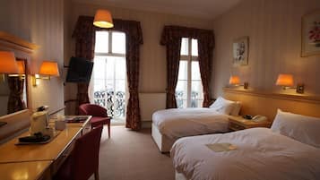 A hotel room with two beds, a desk, a chair, a television, and a window with curtains.