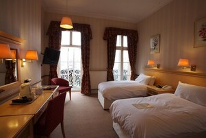 Habitación de hotel con dos camas, un escritorio, una silla, televisión y una ventana con cortinas.