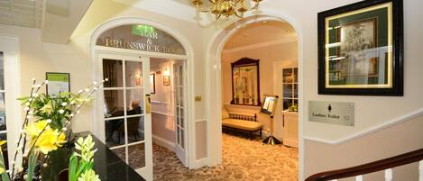 A lobby with a chandelier, a sign for 'Brunswick Room', and a 'Ladies Toilet' sign.