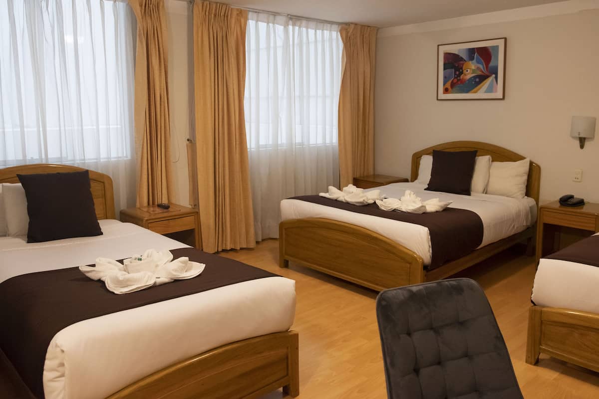 A hotel room with two beds, a wooden headboard, a chair, a painting on the wall, and a window with curtains.