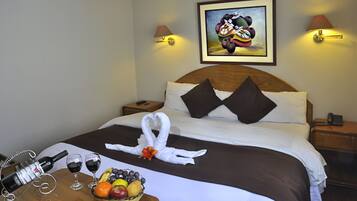 Habitación de hotel con una cama bien hecha, una cesta de frutas, copas de vino y una botella de vino sobre la mesita de noche.